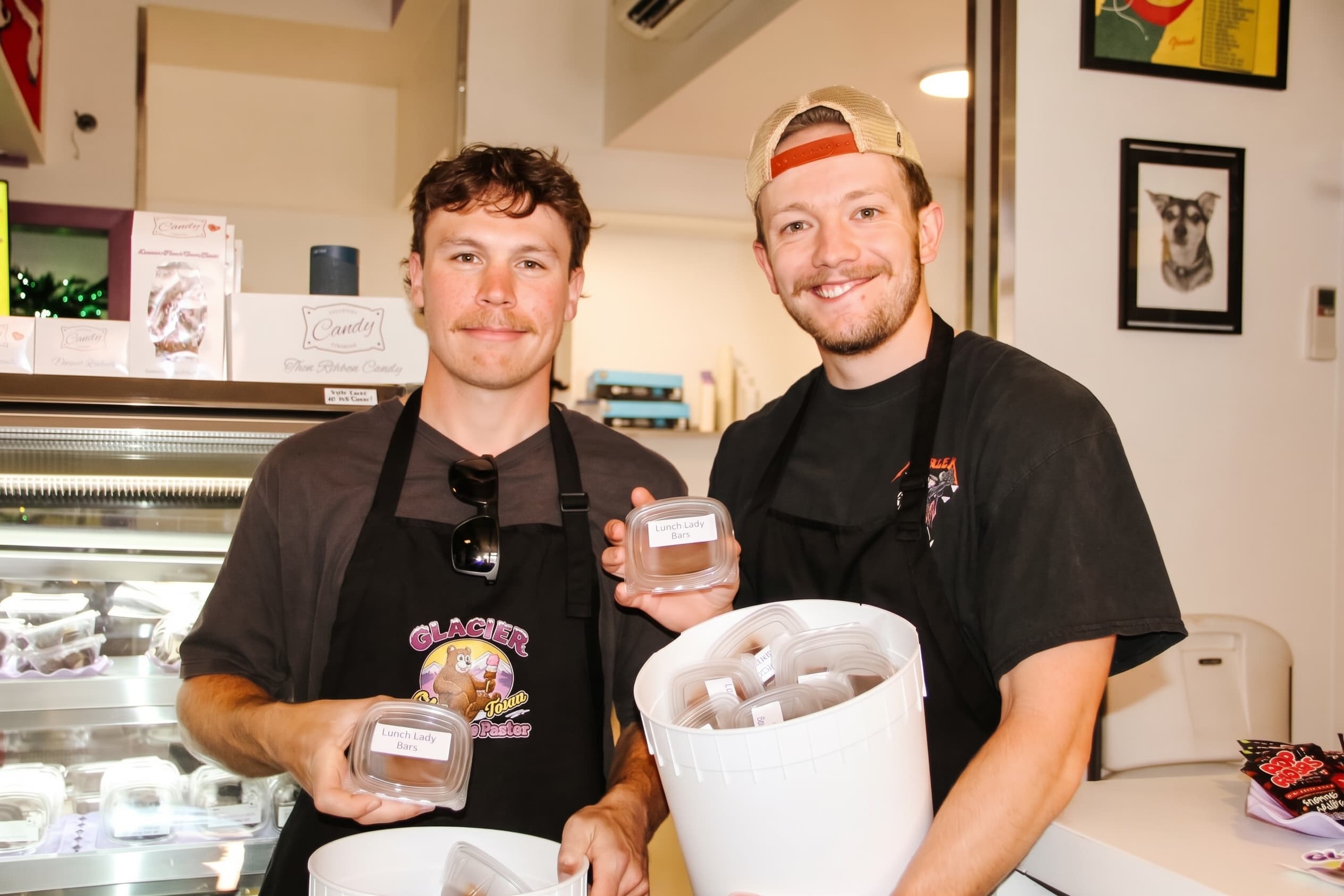 Two scoopers behind the counter holding a fresh tub of ice cream