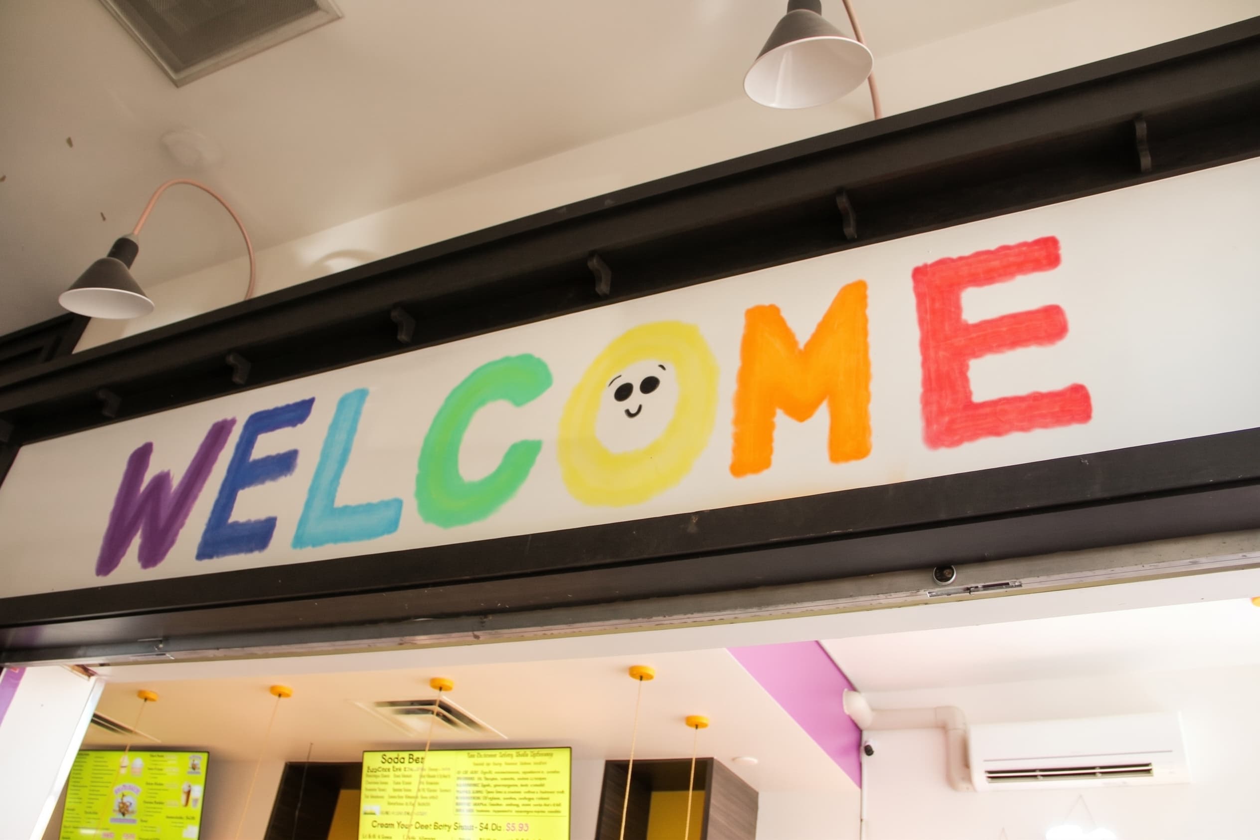The hand-painted rainbow WELCOME letters above the counter