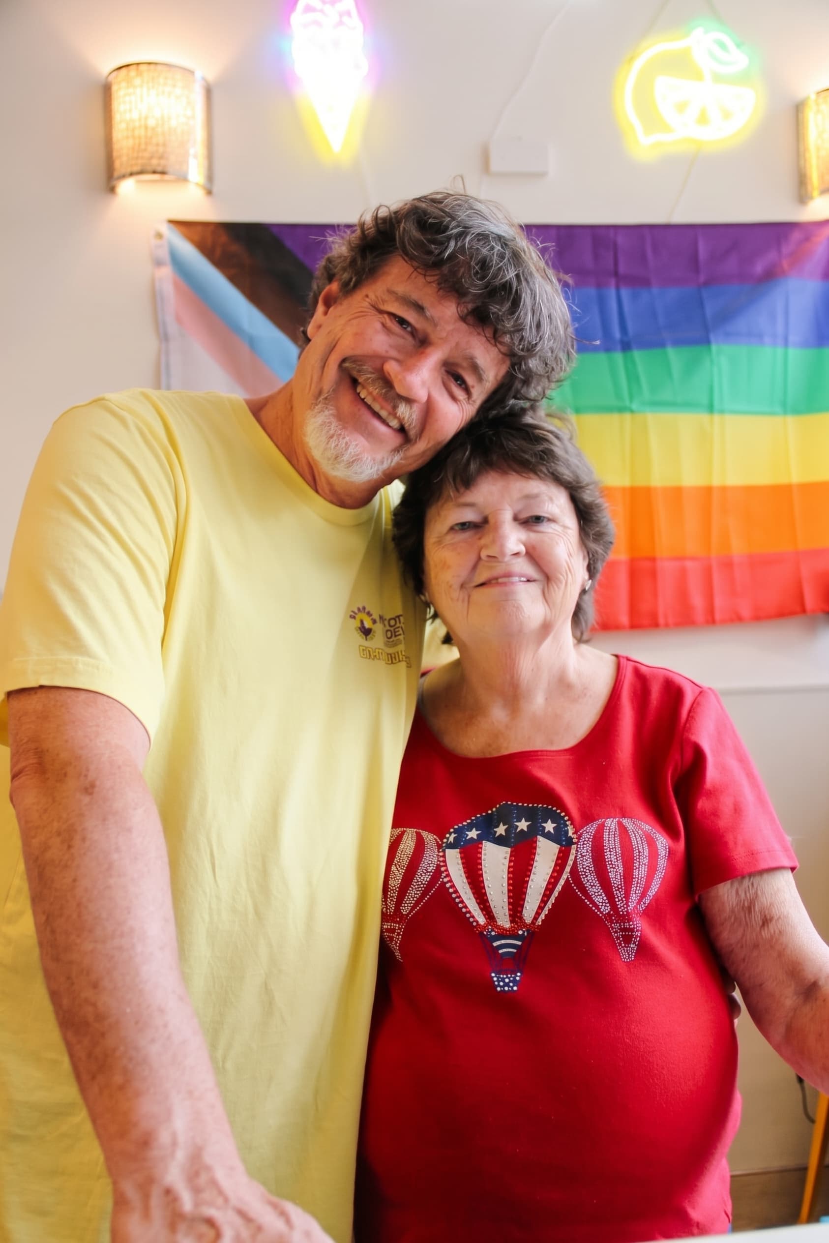 Two guests smiling in front of the pride flag