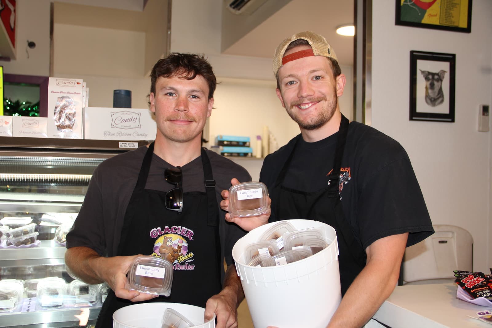 Two scoopers behind the counter holding a fresh tub of ice cream