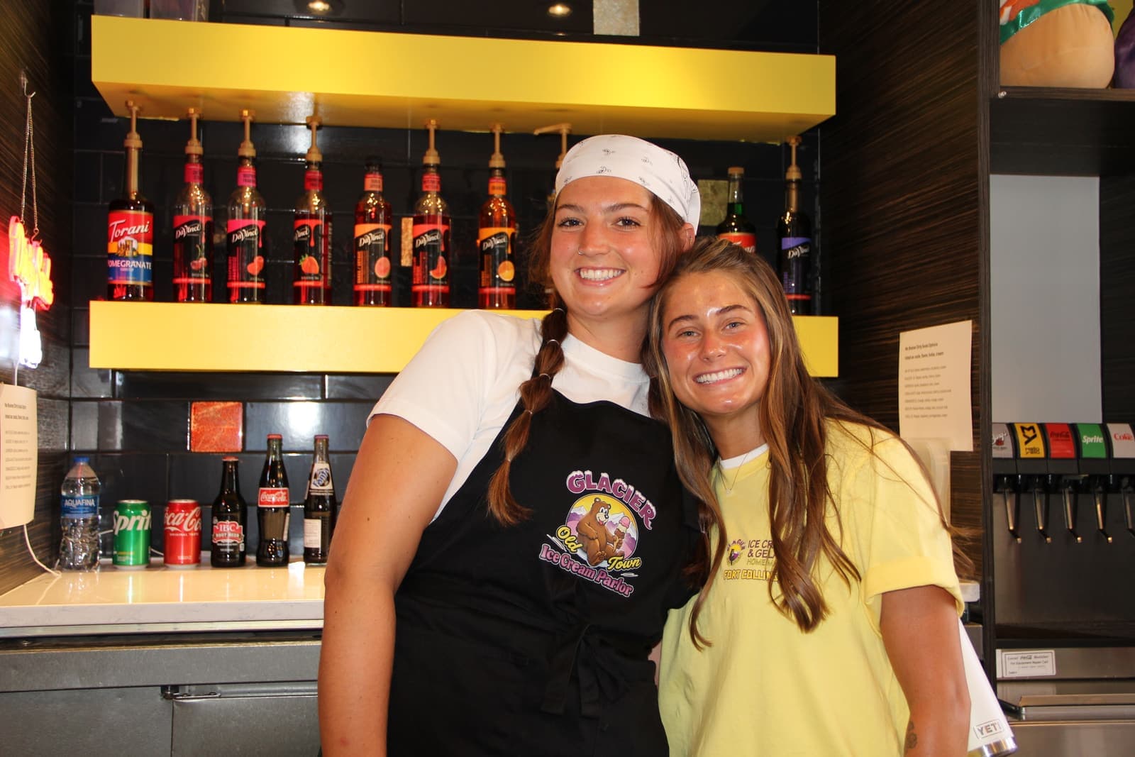 Two crew members behind the soda counter under the syrup shelf