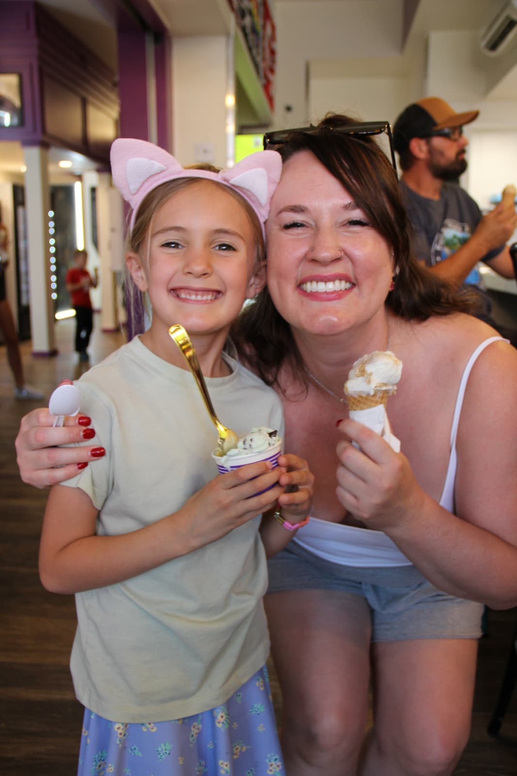 A mom and daughter in cat ears sharing cones