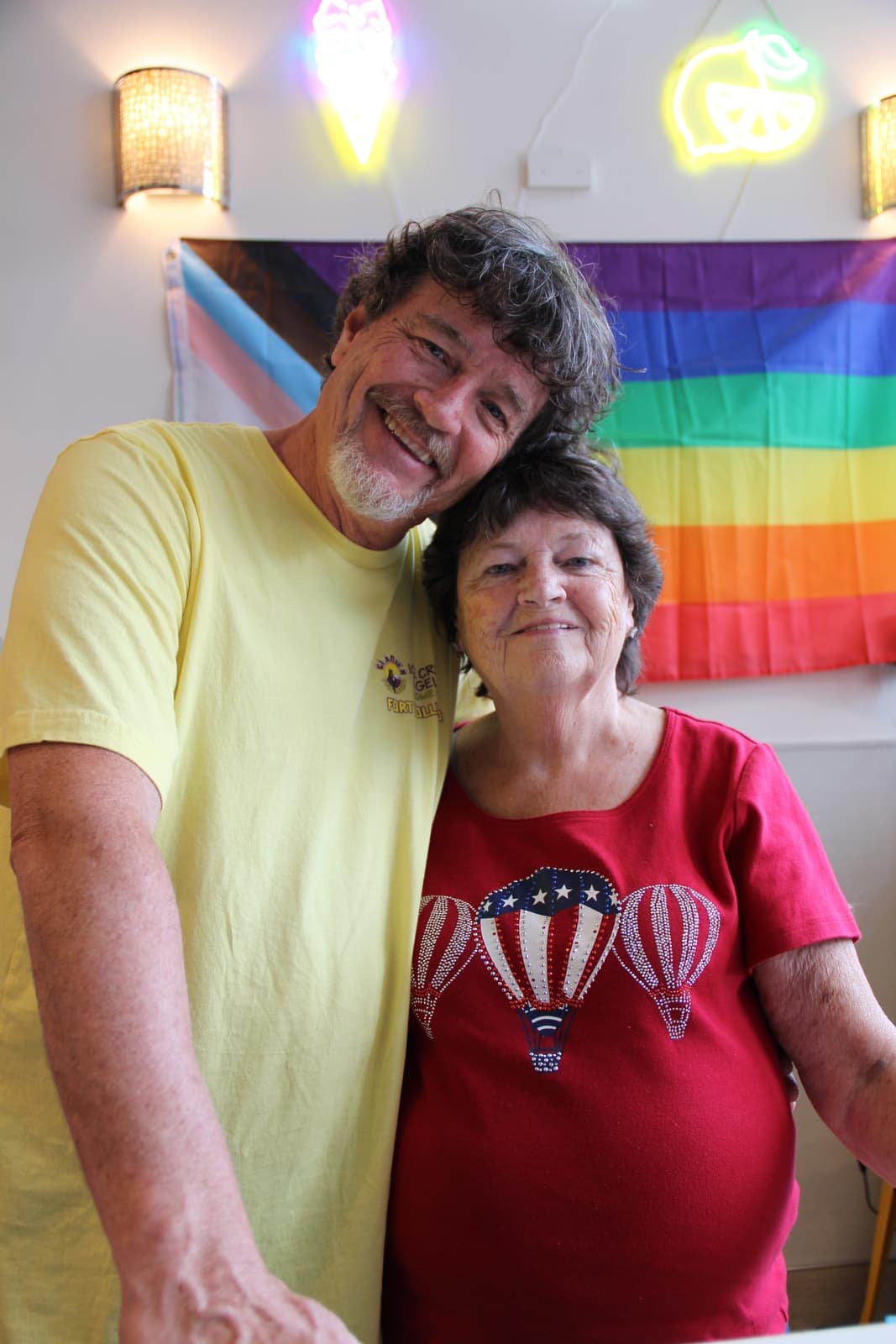 Two guests smiling in front of the pride flag